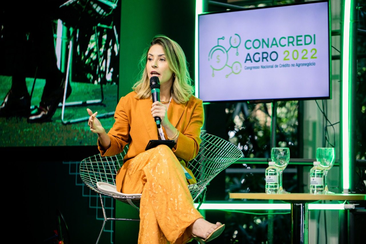 Pauliane Oliveira com microfone em painel do CONACREDI Agro 2022